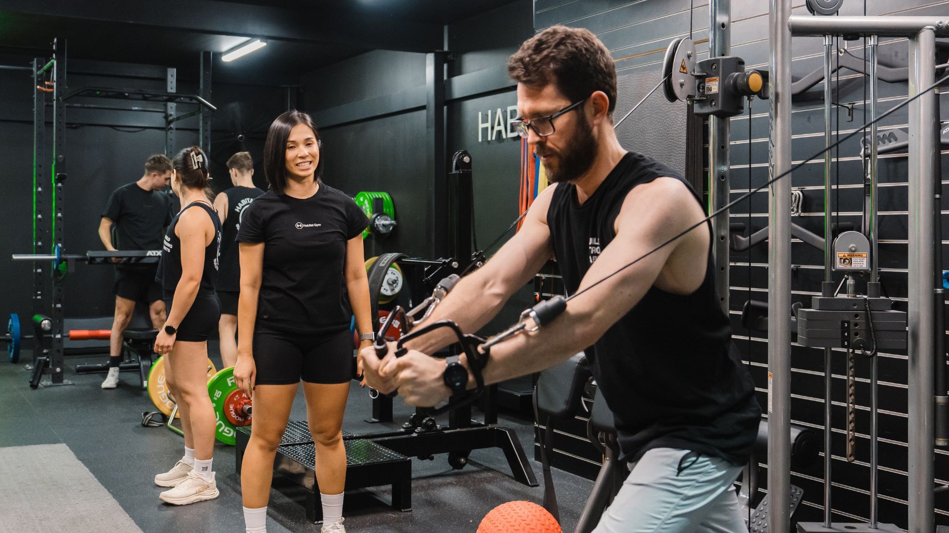 Personal trainer guiding a client in the gym, demonstrating proper form after a break.