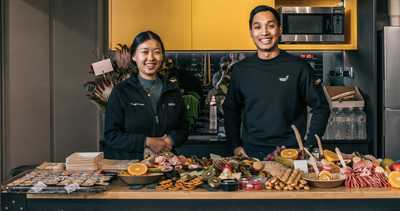 Habitat Gym members posing with a grazing table with fresh fruit, meats and snacks inside the kitchen