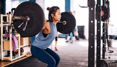 Asian woman performing a barbell squat at the gym, focusing on strength and form.