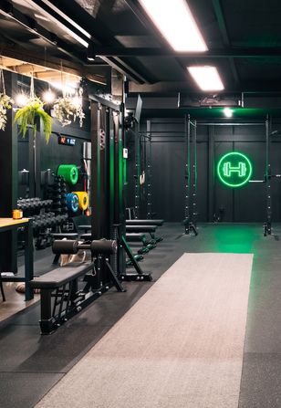 Strength training equipment arranged neatly below the glowing barbell neon sign at Habitat Gym