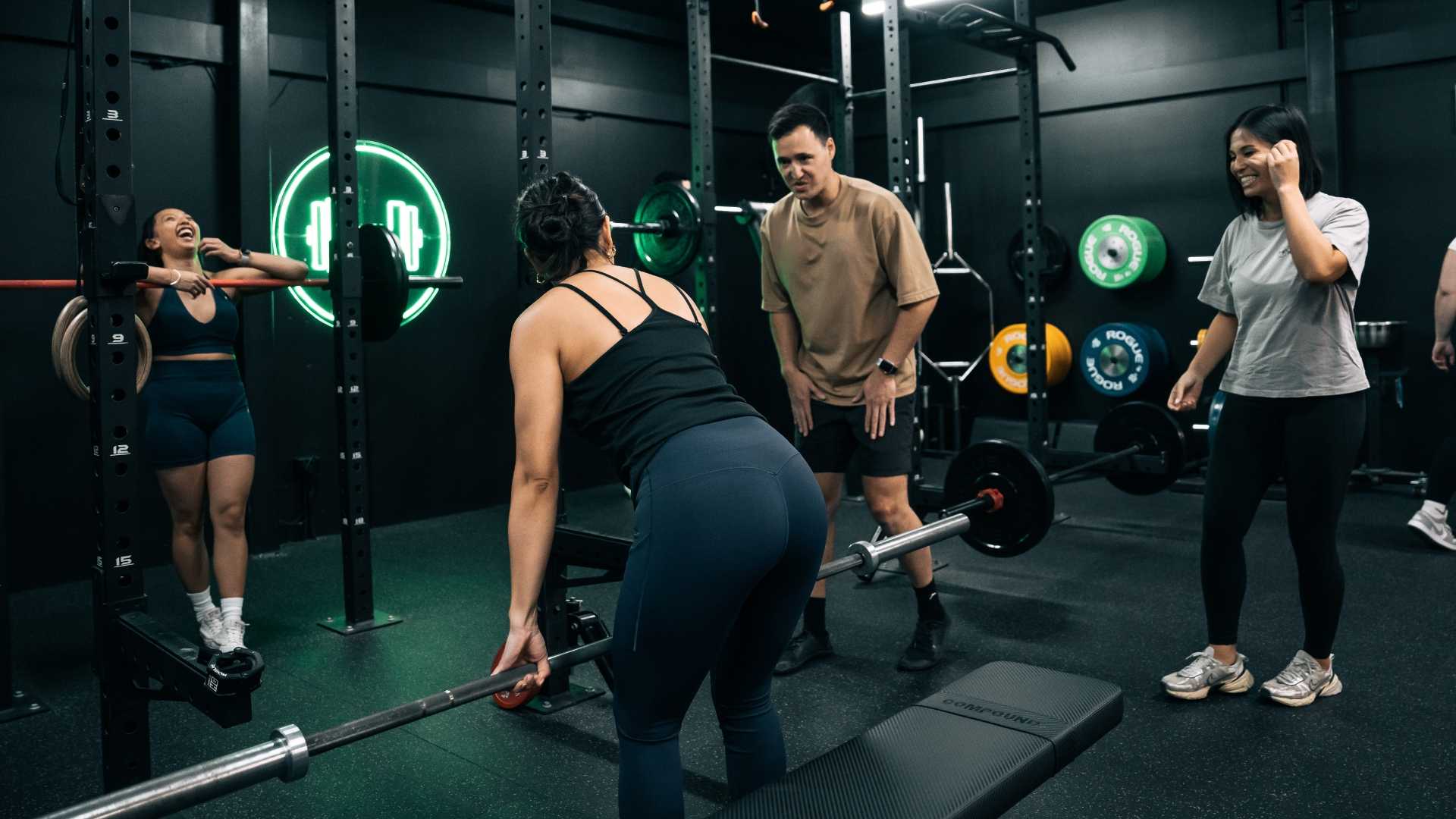Personal trainer guiding a client during a strength training session in the gym, focusing on proper form and technique while other members share an encouraging moment.