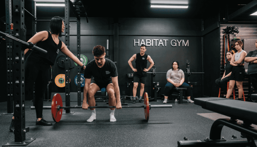 Coach Jeannie correcting gym member's technique whilst lifting weights inside their private gym