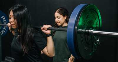 Woman being guided by her trainer in barbell squat training at Habitat Gym